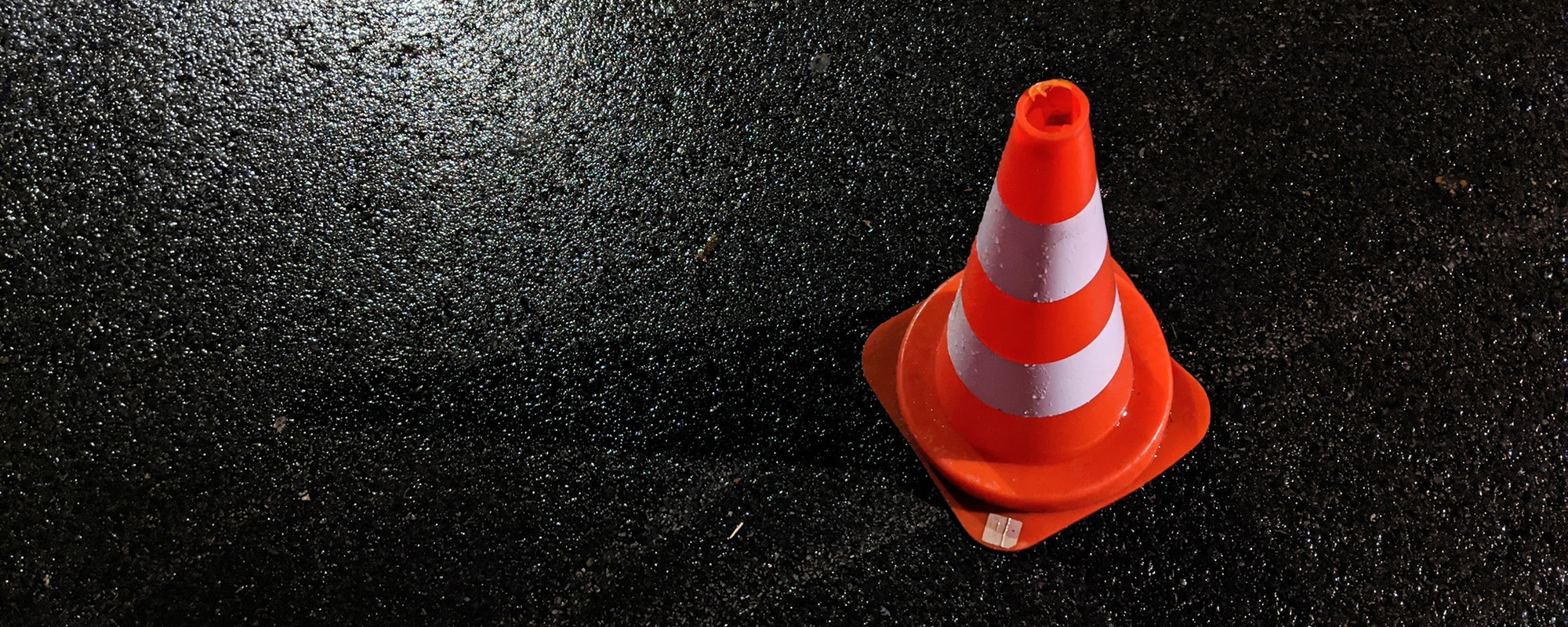 Eine rot-weiß gestreifte Pylone auf nassem Asphalt, umgeben von Reflexionen des Lichts, symbolisiert die Wichtigkeit eines europäischen Unfallprotokolls nach einem Verkehrsunfall. Das Bild steht für Sicherheit an der Unfallstelle, geordnete Schadensregulierung und die Bedeutung einer klaren Dokumentation. Es verdeutlicht, wie ein Unfallprotokoll hilft, wichtige Informationen festzuhalten und die rechtlichen sowie versicherungstechnischen Abläufe zu erleichtern.