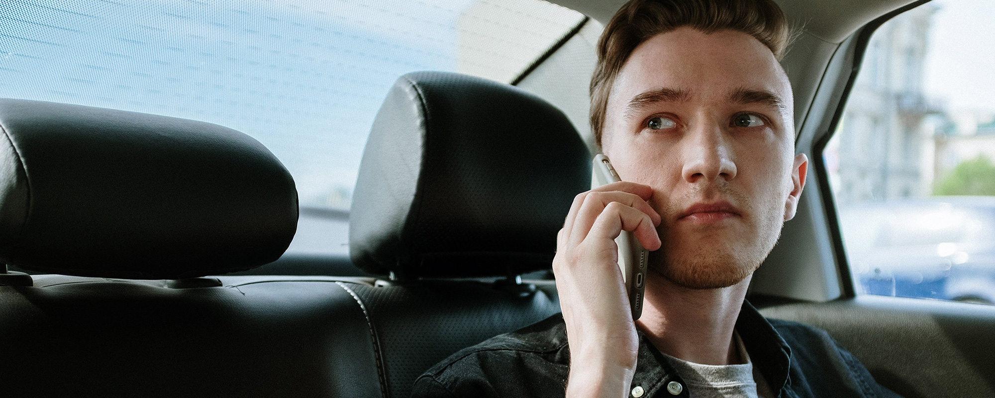 Ein junger Mann sitzt besorgt auf der Rückbank eines Autos und hält sein Handy ans Ohr. Er hat gerade einen Unfall erlebt und sucht Unterstützung über das kostenlose Unfallhilfe-Telefon. Die Hotline für Unfallopfer bietet ihm schnelle Hilfe und zeigt ihm die nächsten Schritte auf. Das Bild symbolisiert schnelle Beratung nach einem Unfall, Orientierung in einer stressigen Situation und die Möglichkeit, unkompliziert Unterstützung zu erhalten.