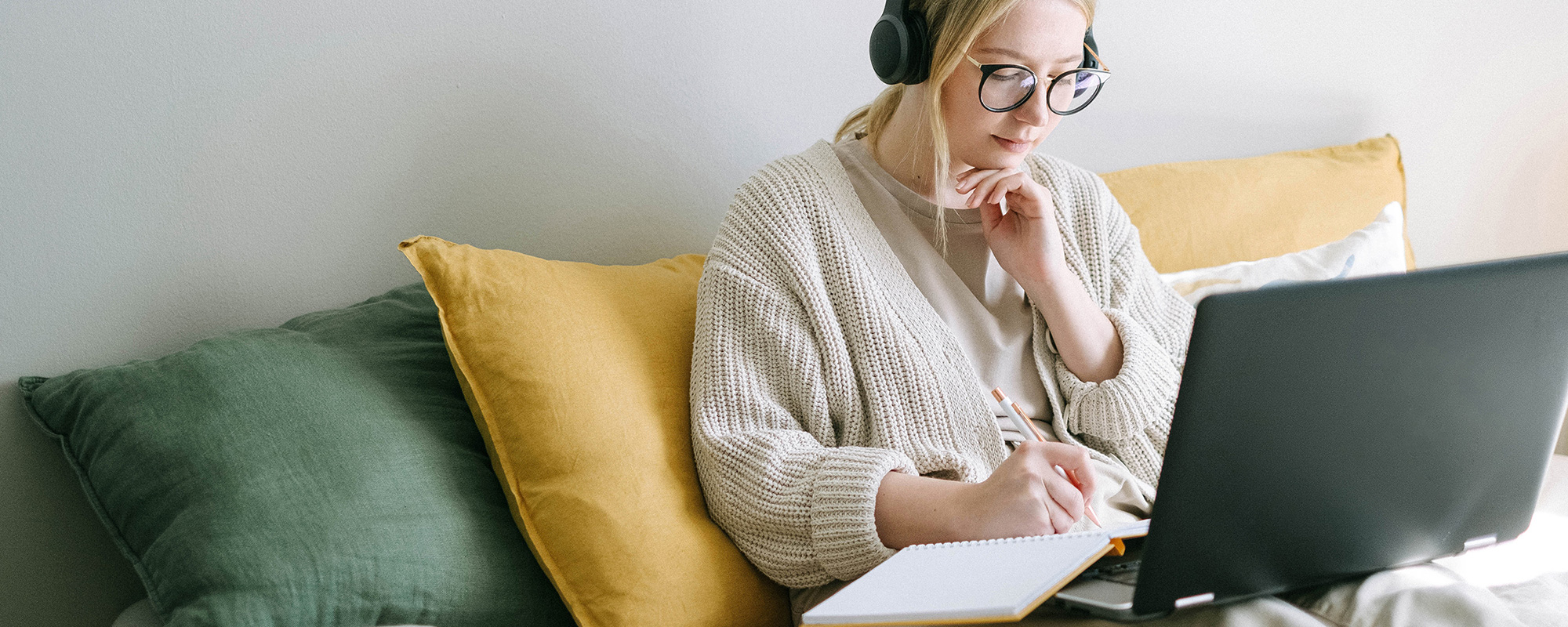 Eine junge Frau mit einer Beinprothese sitzt entspannt in ihrem Bett. Sie trägt Kopfhörer und hört aufmerksam zu, während sie sich konzentriert mit einem Bleistift Notizen in ein offenes Buch macht. Ihr Gesichtsausdruck zeigt Fokus und Interesse – sie hält wichtige Informationen fest, die sie nur durch das **Unfallopfer-Hilfswerk** erhält. Das Bild symbolisiert Zugang zu wertvollem Wissen und Unterstützung für Menschen mit **Handicap**, sei es durch Ratgeber, Podcasts oder persönliche Beratung. Es vermittelt das Gefühl von Selbstbestimmung und der Möglichkeit, durch Wissen neue Perspektiven zu gewinnen.