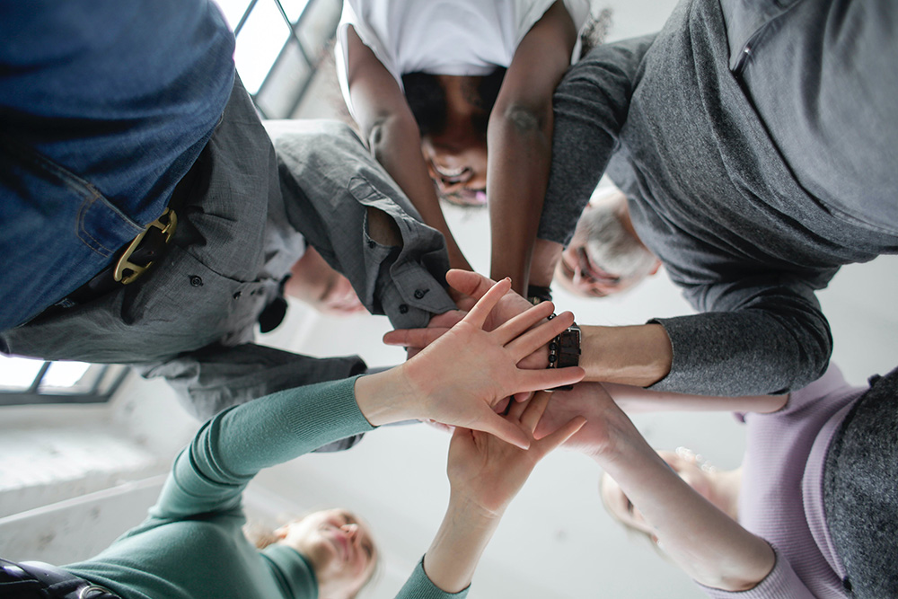 Ein starkes Team für Unfallopfer: Aus der Froschperspektive sind mehrere Menschen zu sehen, die ihre Hände in der Mitte aufeinanderlegen – ein Symbol für Zusammenhalt, Unterstützung und Engagement. Das Team des Unfallopfer-Hilfswerks setzt sich mit Leidenschaft für die Unterstützung von Unfallopfern ein. Mit ihrer Erfahrung und Empathie helfen sie Betroffenen dabei, nach einem Unfall wieder Fuß zu fassen. Gemeinsam stehen sie für Inklusion, Gerechtigkeit und Teilhabe und zeigen, dass niemand mit seinen Herausforderungen allein ist. Ihre Aufgabe ist es, Wege aufzuzeigen und Unfallgeschädigten zu helfen, ihr Leben wieder selbstbestimmt zu gestalten.