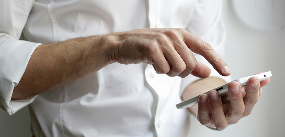 Datenschutz - Unfallopfer Hilfswerk GmbH: Ein Mann in einem weißen Hemd hält ein Smartphone in der Hand und liest die Datenschutzbestimmungen. Sein konzentrierter Blick unterstreicht die Wichtigkeit des verantwortungsvollen Umgangs mit persönlichen Daten. Das Bild symbolisiert das Engagement des Unfallopfer-Hilfswerks für Datenschutz, Transparenz und die sichere Verarbeitung sensibler Informationen gemäß den gesetzlichen Vorgaben.